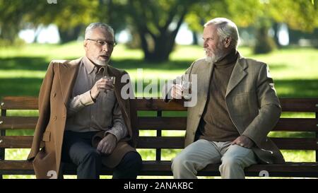 Two serious old gentlemen drinking whiskey, enjoying beautiful day in park Stock Photo