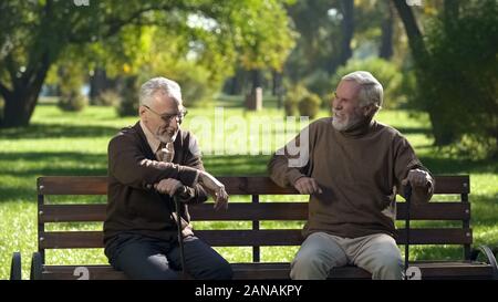 Two senior friends laughing and remembering past days spending time in park Stock Photo