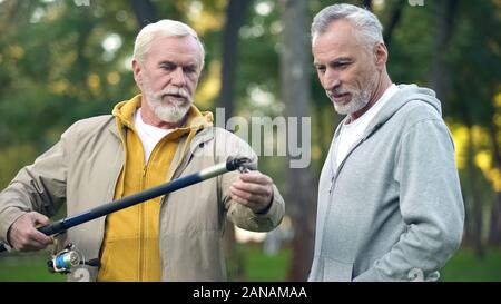 Aged male showing new fishing rod to friend, pensioner hobby, togetherness Stock Photo