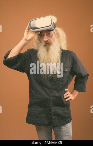 Studio shot of senior bearded man wearing black shirt against brown background Stock Photo