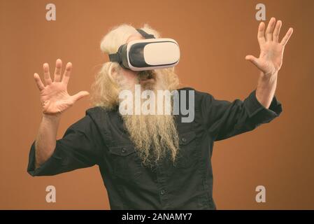 Studio shot of senior bearded man wearing black shirt against brown background Stock Photo