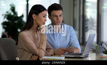 Male and female colleagues looking laptop in office, working at project together Stock Photo
