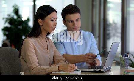 Young man teaching female trainee use laptop program, office job, cooperation Stock Photo