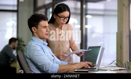 Young business partners working on project together, comparing details on laptop Stock Photo