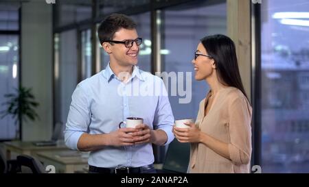 Smiling man and woman talking during break holding coffee cups, colleagues Stock Photo