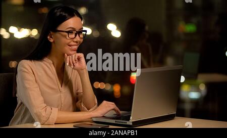 Smiling young woman watching online video on laptop, reading email, freelancer Stock Photo