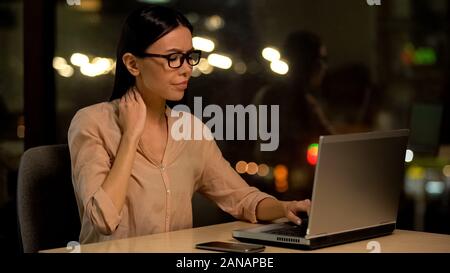 Tired business lady feeling neck pain working on laptop at night, health care Stock Photo