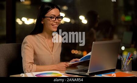 Creative designer reviewing color palette using laptop, enjoying favorite job Stock Photo