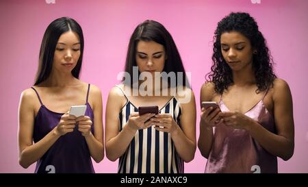 Women chatting on smartphone instead of having fun during pajama party, addict Stock Photo