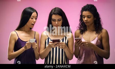 Girls with smartphones looking female friend texting message, pink background Stock Photo