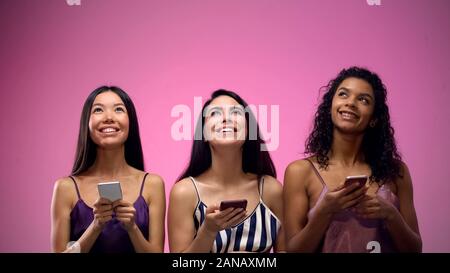 Three adorable multiracial women using mobile apps and looking up, template Stock Photo