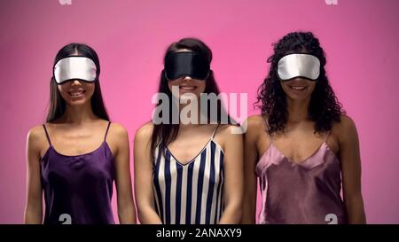 Smiling multiracial women in pajamas wearing eye masks, ready to sleep, relax Stock Photo