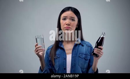 Thirsty woman choosing what to drink between fresh and fizzy water, decision Stock Photo