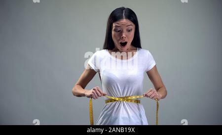 Obsessed woman tightening measuring tape on her waist desire to be slim, bulimia Stock Photo