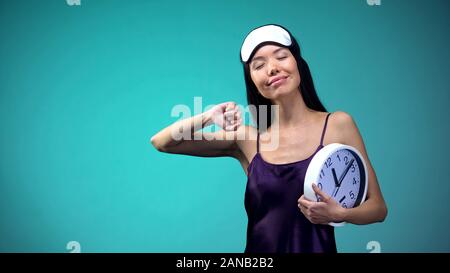 Smiling woman stretching in morning and holding clock, late awakening, energy Stock Photo