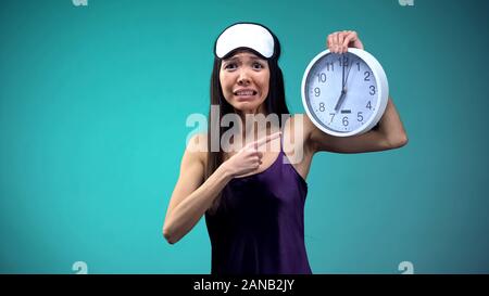Frustrated girl pointing at 7 am on clock face, overslept and getting late Stock Photo