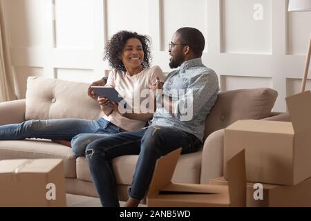 Smiling black family couple sitting on couch with tablet. Stock Photo