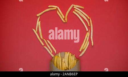 Crispy french fries heart shape symbol on red background, fast food, charity Stock Photo