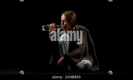 Miserable alcohol addicted woman drinking vodka from bottle in darkness, addict Stock Photo