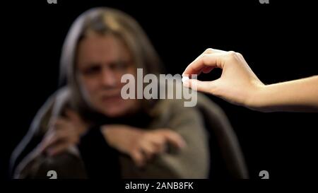 Hand offering LCD pill to woman suffering withdrawal symptoms, drug addiction