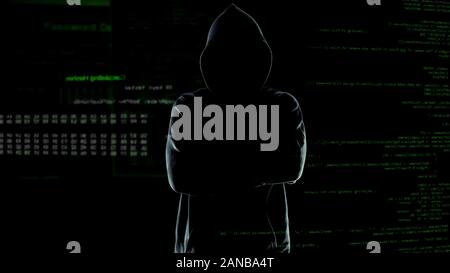 Anonymous hacker in hoodie with arms crossed on numbers and codes background Stock Photo