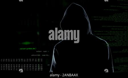 Faceless male hacker in hoodie standing in front of animated computer code Stock Photo