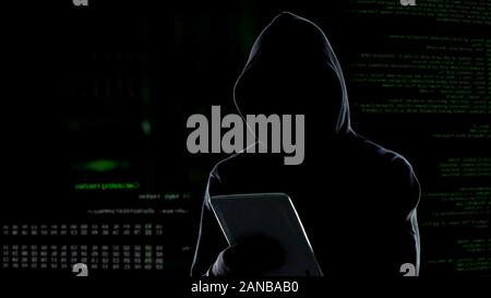 Cyber attack with unrecognizable hooded hacker using tablet computer, cybercrime Stock Photo