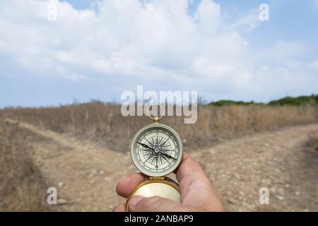 Man holding a compass on a fork in the road on a decision, dilemma, direction concept Stock Photo