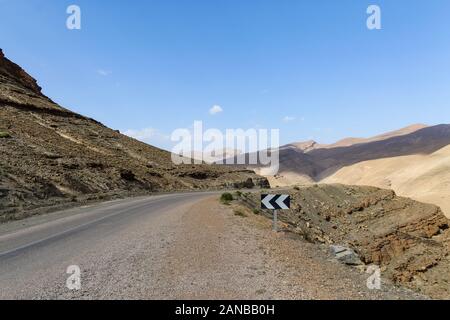 Empty road in southern Morocco with blue skies and mountains in the background Stock Photo