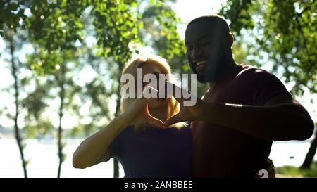 Amorous mixed race couple showing heart shape with hands, interracial marriage Stock Photo