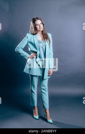 Attractive woman dressed in blue suit on grey background. Women's business suits concept. Posing in studio Stock Photo