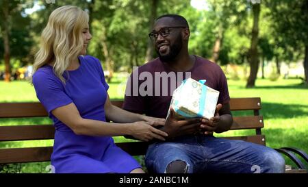 Afro-American man getting surprise present from female friend in park, b-day Stock Photo