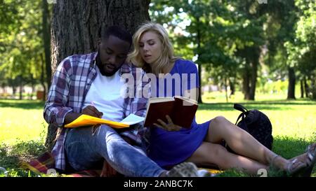 Mixed raced students making notes and looking in book, university project Stock Photo