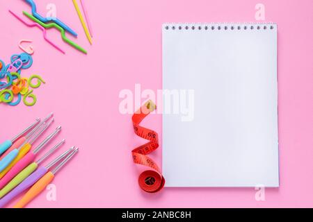 Top view of white empty notebook with crocheting and knitting accessories on soft pink background Stock Photo