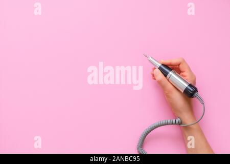 Woman hand holding electric nail manicure machine pen on pink background Stock Photo