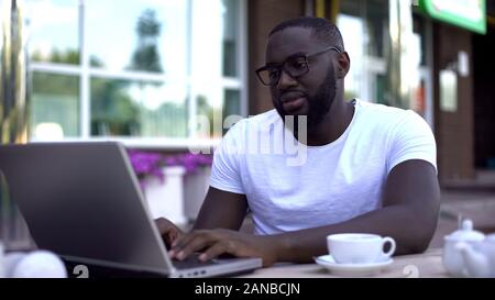 Disappointed man checking email on laptop pc in outdoor cafe, receiving bad news Stock Photo