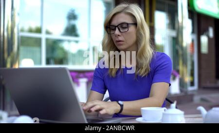 Successful businesswoman working on laptop, sitting in cafe terrace, workaholic Stock Photo