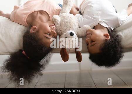 Happy black brother and sister laying upside down on bed. Stock Photo