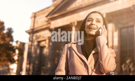 Beautiful young lady talking on smartphone, standing near classical building Stock Photo