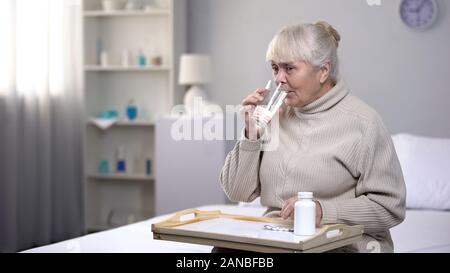 Senior lady taking pills and drinking water in rehabilitation center, healthcare Stock Photo