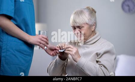 Nurse giving painkillers elderly woman suffering from headache, taking care Stock Photo