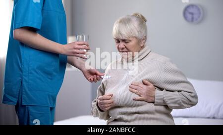Medical worker giving pills elderly lady suffering from heart pain, treatment Stock Photo