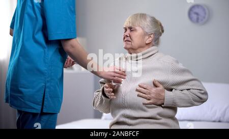 Nurse giving pain killers elderly lady suffering from heart attack, treatment Stock Photo