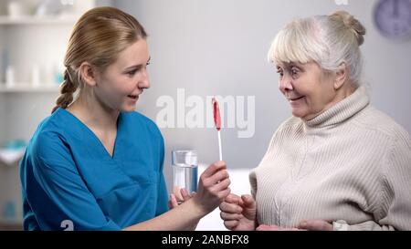 Nurse giving medical pills and lollipop to old woman, taking care about patient Stock Photo