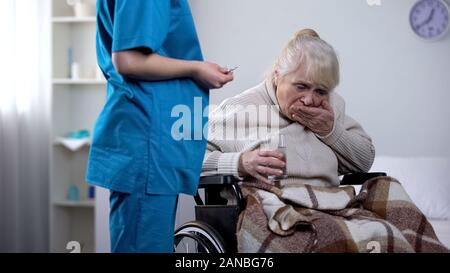 Young nurse giving medications to old lady in wheelchair, rehabilitation center Stock Photo