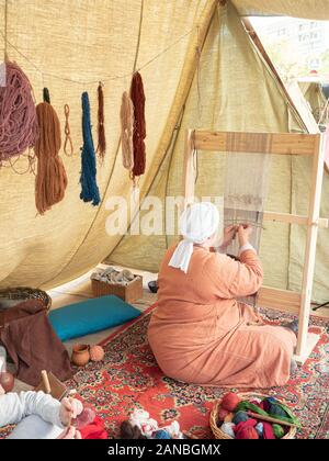 Times and Epochs Festival. Female Weaver Weaves a Canvas With a Pattern of Wool Yarn. Woman Weaves Using a Traditional Wooden Loom Stock Photo