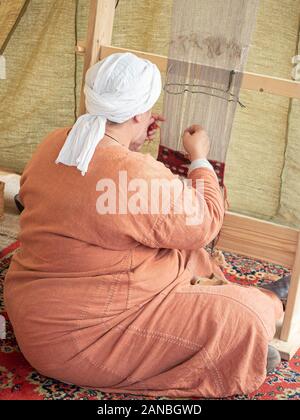 Times and Epochs Festival. Female Weaver Weaves a Canvas With a Pattern of Wool Yarn. Woman Weaves Using a Traditional Wooden Loom Stock Photo