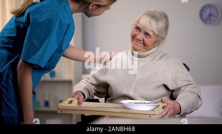 Medical worker taking care of aged female patient, gently care in nursing home Stock Photo