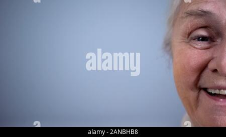 Half-face of positive elderly female on grey background, cheerful pensioner Stock Photo