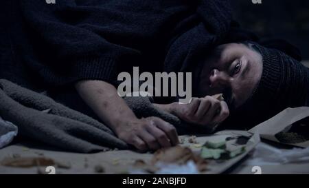 Sick hungry homeless person lying on street and eating last piece of orts Stock Photo